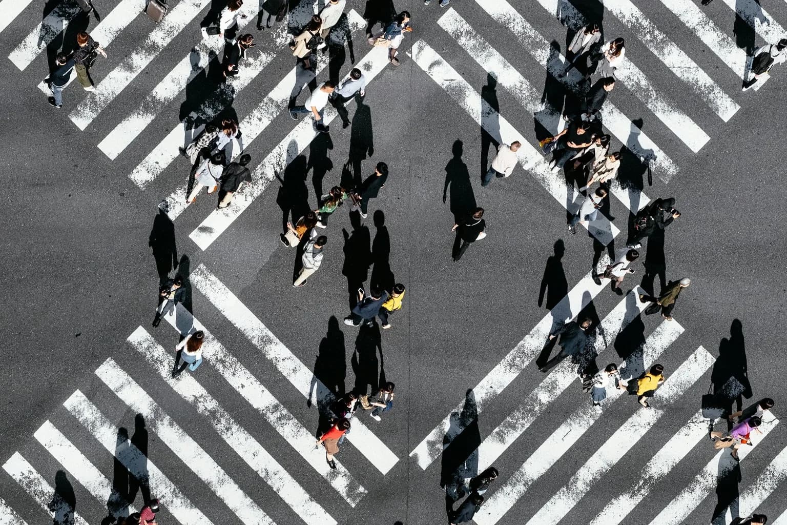 People crossing intersecting pedestrian crossings viewed from above.